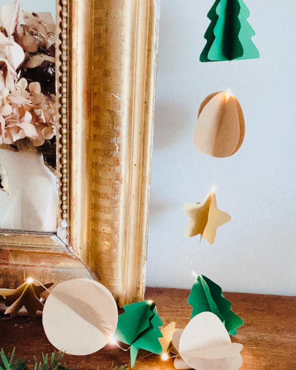 Guirlande de Noël artisanale décorée de sapins, étoiles et formes rondes en papier. La lumière LED met en valeur les détails délicats du travail manuel. Une idée de décoration chaleureuse, naturelle et raffinée, conçue pour illuminer la maison pendant les fêtes. ninona