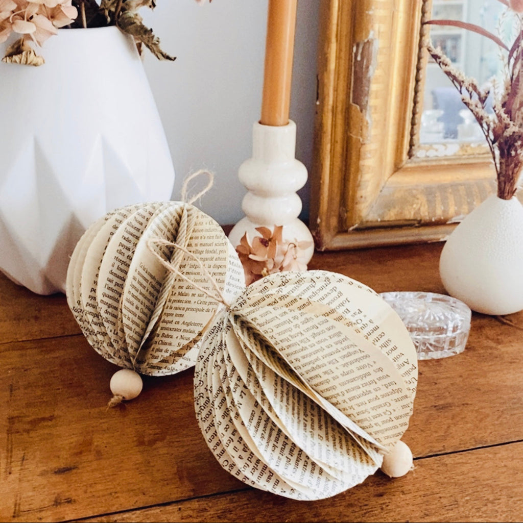 Ces boules légères sont nées de pages oubliées, patinées par le temps. Chaque feuille de vieux livre a été découpée, pliée et assemblée à la main, révélant une douce harmonie entre papier ancien, ficelle naturelle et perle de bois. Parfaites pour une décoration poétique et durable, elles apportent une touche d’authenticité et de charme à tout intérieur. ninona