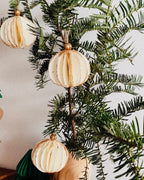 Boules de Noël écru suspendues à une branche de sapin, dévoilant leur forme ronde, légère et texturée. Les paillettes dorées ajoutent une touche scintillante discrète et élégante. L’ensemble crée une ambiance décorative naturelle, apaisante et raffinée, idéale pour une décoration de Noël minimaliste et chaleureuse. ninona