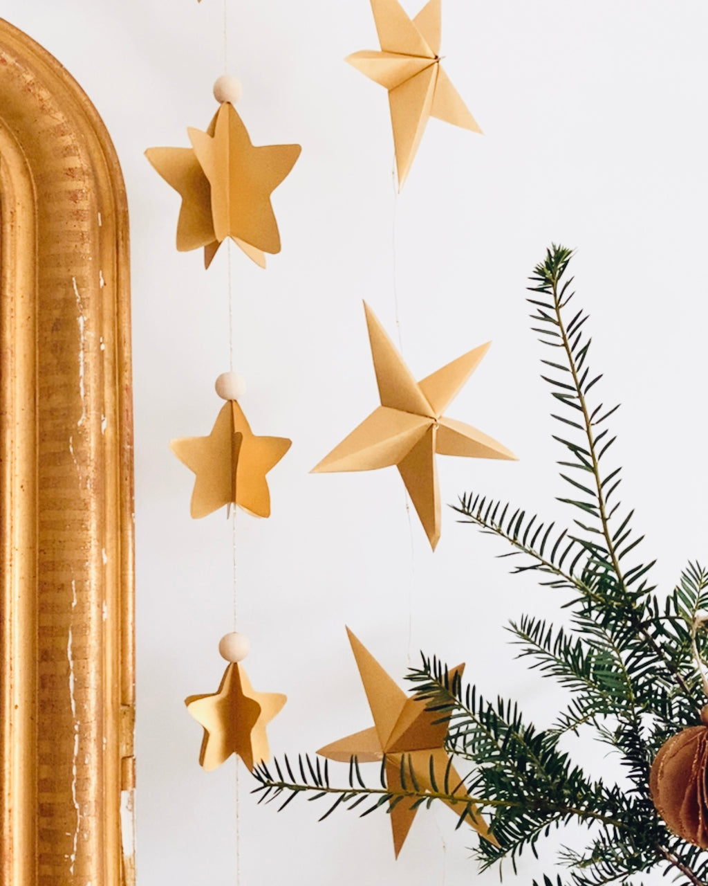 Guirlande d’étoiles en papier doré fixée près d’un miroir ancien. Lumière LED douce créant une ambiance chaleureuse et accueillante. Chaque étoile est réalisée à la main avec soin, inspirée de l’artisanat et de la décoration naturelle. Parfait pour le salon, une chambre d’enfant, ou pour créer une atmosphère de Noël douce et lumineuse. Décoration élégante et poétique. ninona