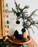 Composition festive réunissant boules de Noël artisanales, plateau en bois et branches de sapin naturel. Le décor évoque la simplicité d’un Noël fait maison, avec des matières naturelles, du papier, du bois et de fines touches dorées. L’ensemble transmet une ambiance calme, chaleureuse et poétique. ninona