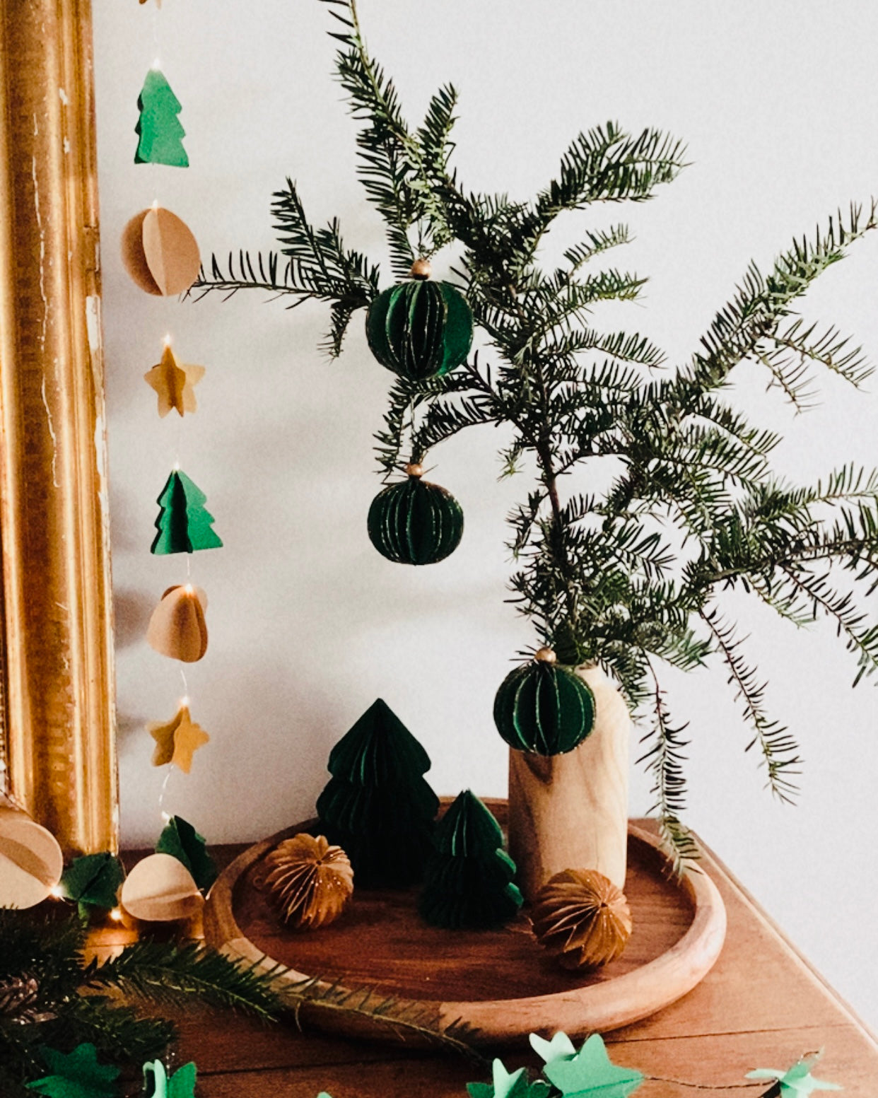 Composition festive réunissant boules de Noël artisanales, plateau en bois et branches de sapin naturel. Le décor évoque la simplicité d’un Noël fait maison, avec des matières naturelles, du papier, du bois et de fines touches dorées. L’ensemble transmet une ambiance calme, chaleureuse et poétique. ninona
