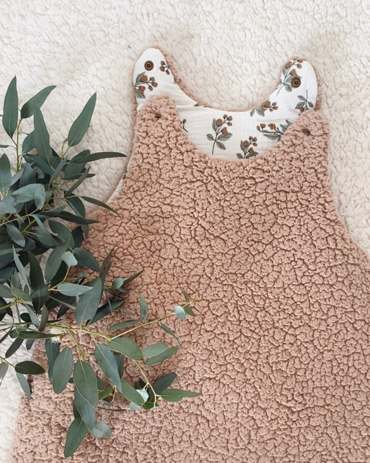 Zoom sur le haut de la gigoteuse bébé hiver en sherpa, taille 0/6 mois. À l’intérieur, la double gaze de coton blanc cassé se pare de motifs végétaux délicats aux nuances brunes et vertes. Une création cocooning et chaleureuse, idéale pour garder bébé bien enveloppé durant les nuits fraîches, avec une finition soignée et pleine de douceur. Une jolie création bébé, douce. Ninona