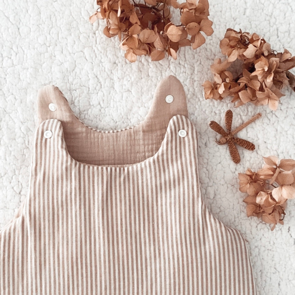 Gigoteuse bébé artisanale à rayures beige et écru, confectionnée avec soin à la main. Son style doux et intemporel s’accorde parfaitement à l’univers de bébé. Cette gigoteuse personnalisable peut être réalisée selon vos envies et convient aux filles comme aux garçons. Disponible en plusieurs tailles et en trois versions : été, mi-saison ou hiver, elle accompagne bébé au fil des saisons dans un cocon confortable et douillet. Idée cadeau de naissance originale et personnalisée. Ninona