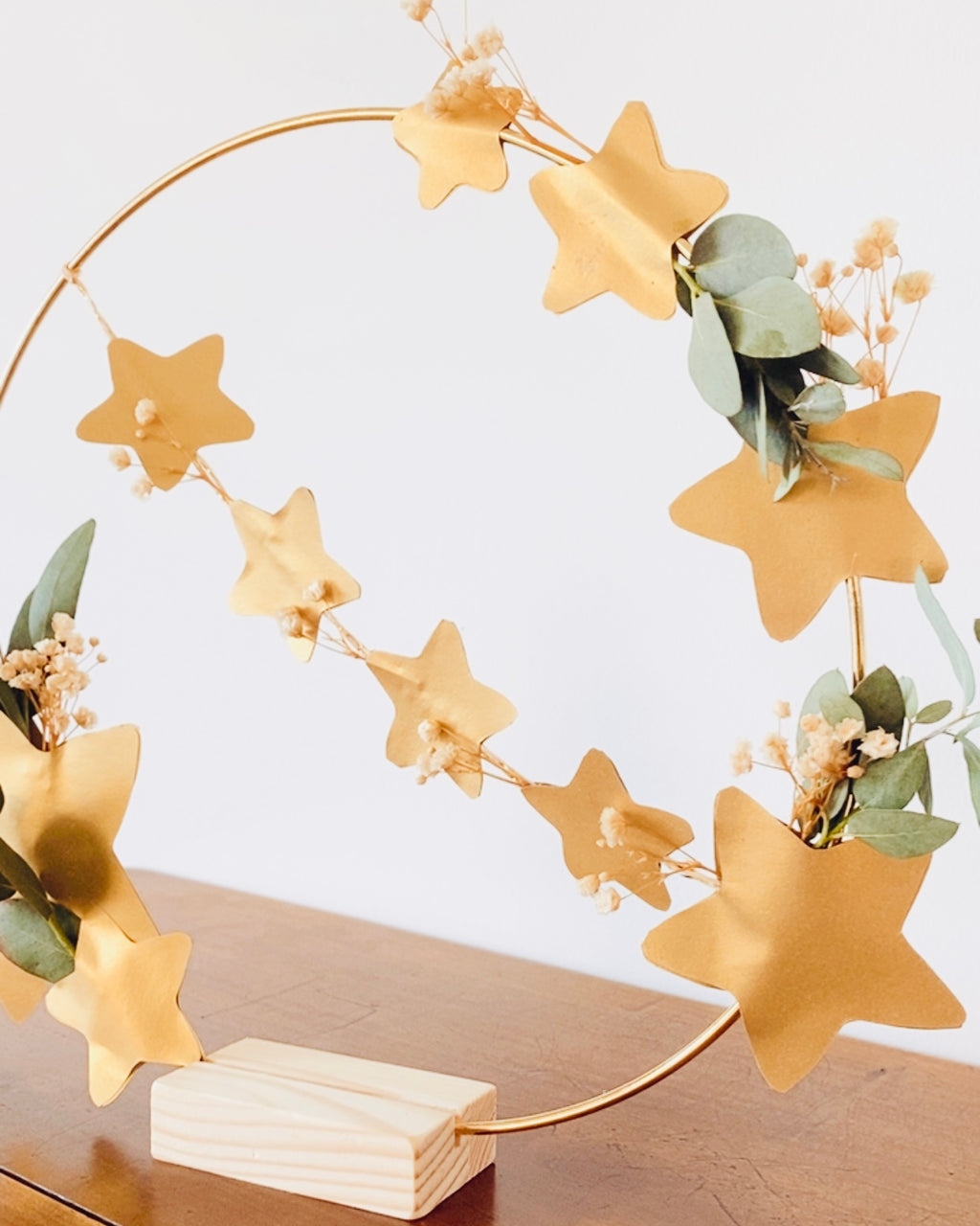 Couronne poétique réalisée à la main, composée de fleurs séchées blanches, de feuilles d’eucalyptus et d’étoiles dorées montées sur un cerceau métallique. Peut être suspendue au mur ou posée grâce à son socle en bois. Décoration artisanale made in France, parfaite pour Noël, une entrée, une chambre ou un salon. Idée cadeau créative pour celles et ceux qui aiment la décoration naturelle, minimaliste et chaleureuse. ninona
