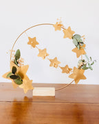 Couronne florale délicate avec eucalyptus et petites fleurs séchées, décorée d’étoiles dorées. Fait main en France, avec soin et attention portée aux détails. Peut être suspendue ou utilisée comme décoration de table avec son socle en bois. Adaptée à la décoration de maison, aux fêtes de fin d’année, à un intérieur bohème ou scandinave. Cadeau chaleureux, durable et symbolique pour Noël ou une occasion spéciale. ninona