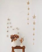 Sur un fil de jute, les étoiles en papier d’anciens livres s’égrènent comme un poème. Leurs reliefs captent la lumière et révèlent la beauté simple du fait main. Entre pages froissées et perles de bois, cette guirlande de 185 cm apporte chaleur et authenticité à chaque coin de maison. Une ode à la douceur et au temps retrouvé. ninona