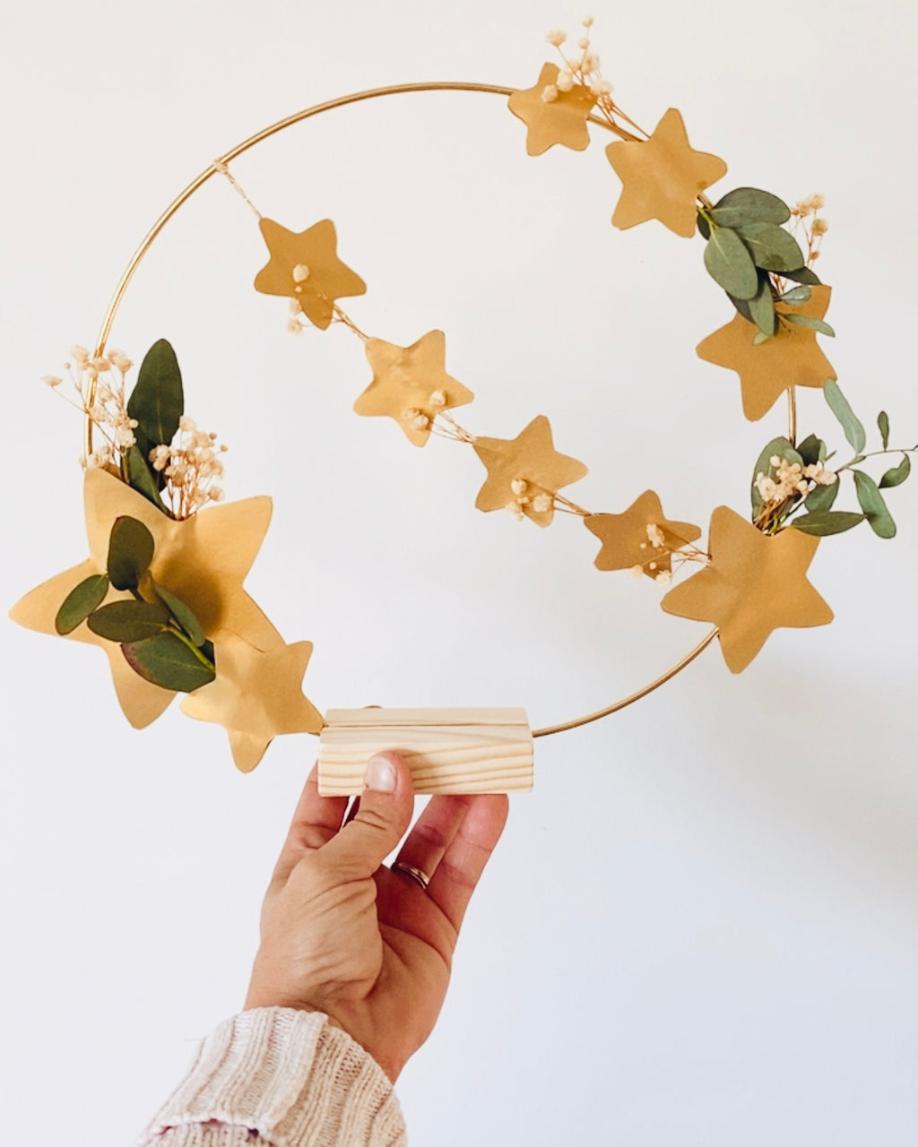 Anneau décoratif doré orné de fleurs séchées et d’eucalyptus, agrémenté d’étoiles dorées découpées à la main. Style naturel et poétique. Création artisanale française pouvant être accrochée ou posée sur un socle. Idéale pour une décoration de Noël douce et minimaliste ou pour sublimer un intérieur toute l’année. Excellent choix de cadeau fait main, durable, attentionné et unique. ninona