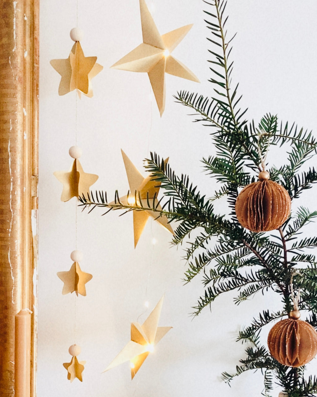 Guirlande d’étoiles en papier doré fixée près d’un miroir ancien. Lumière LED douce créant une ambiance chaleureuse et accueillante. Chaque étoile est réalisée à la main avec soin, inspirée de l’artisanat et de la décoration naturelle. Parfait pour le salon, une chambre d’enfant, ou pour créer une atmosphère de Noël douce et lumineuse. Décoration élégante et poétique. ninona