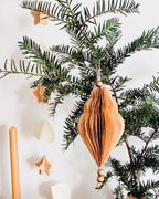 Décoration de Noël artisanale en papier, suspendue par une cordelette naturelle avec une perle dorée. La boule présente une forme élégamment travaillée en plusieurs couches découpées à la main, avec de légères touches de paillettes dorées qui soulignent ses contours. L’ornement, de teinte écru douce, est tenu dans une main, mettant en valeur son relief, sa finesse et son allure poétique, idéale pour décorer un sapin ou une guirlande de fête. ninona