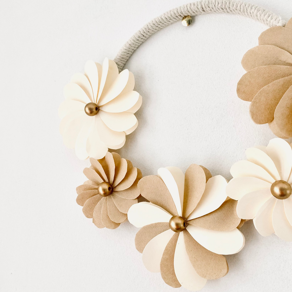 Couronne décorative artisanale composée de fleurs en papier écru et en filtres à café, façonnées pétale par pétale. Les perles de bois cuivrées apportent une touche élégante et lumineuse. Son style naturel et délicat convient aux décorations bohèmes, minimalistes ou scandinaves. Cette pièce unique de 20 cm peut être suspendue dans un salon, une chambre ou utilisée pour un mariage ou un shooting photo. ninona