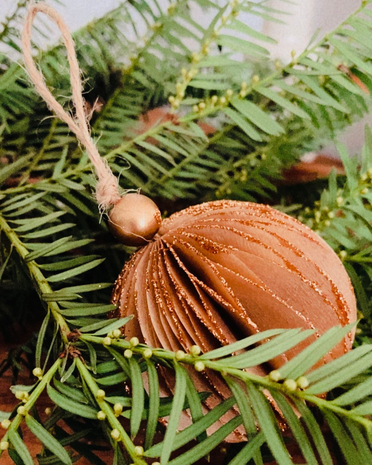 Lot de trois boules de Noël marron posées dans un plateau ou sur une table en bois, entourées de branches de sapin naturelles. L’atmosphère est douce, rustique et chaleureuse, évoquant une décoration de fêtes naturelle et artisanale. Les paillettes apportent une touche délicate de lumière et de magie. ninona