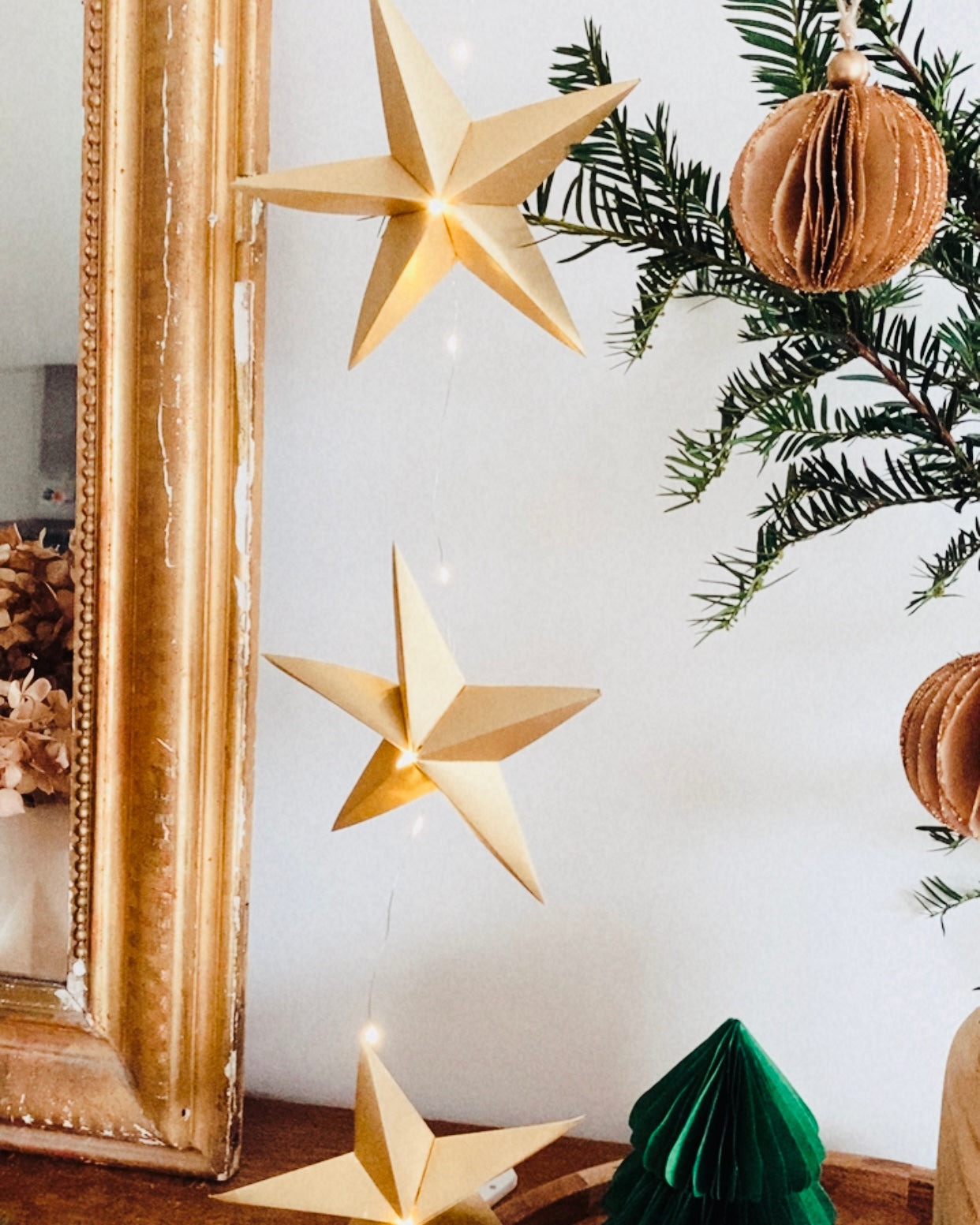 Guirlande d’étoiles en papier doré fixée près d’un miroir ancien. Lumière LED douce créant une ambiance chaleureuse et accueillante. Chaque étoile est réalisée à la main avec soin, inspirée de l’artisanat et de la décoration naturelle. Parfait pour le salon, une chambre d’enfant, ou pour créer une atmosphère de Noël douce et lumineuse. Décoration élégante et poétique. ninona