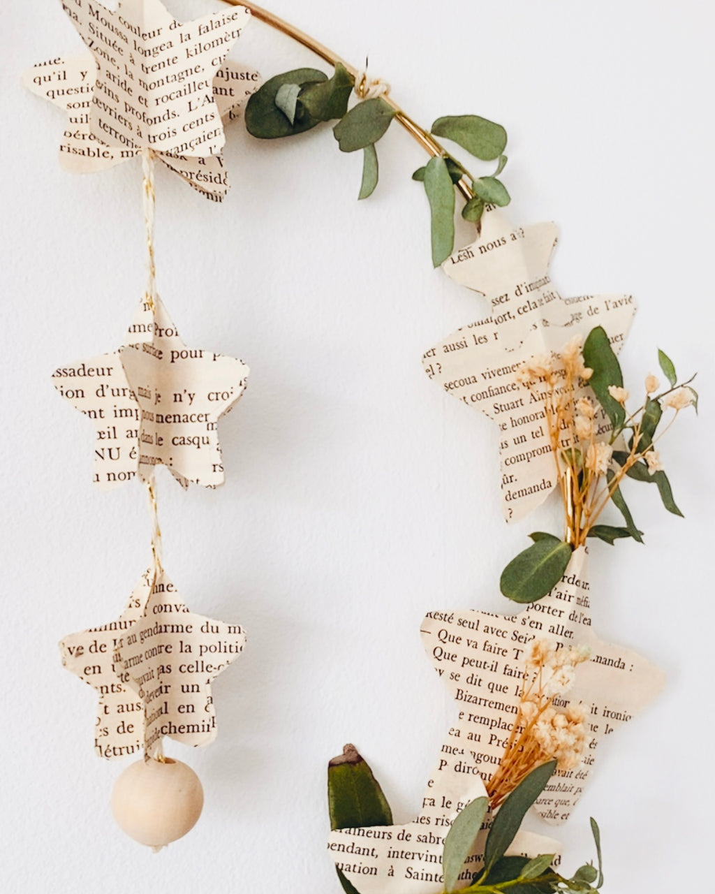 Couronne poétique et écologique en papier recyclé et végétaux séchés, parfaite pour décorer la maison avec délicatesse. Ses étoiles en papier de livre rappellent les objets vintage et empreints d’histoire, tandis que les fleurs et feuilles séchées ajoutent une touche végétale naturelle. Idéale en décoration de Noël ou comme décoration murale en toute saison. Fabriquée à la main en France, chaque pièce est unique et chargée de sens. ninona