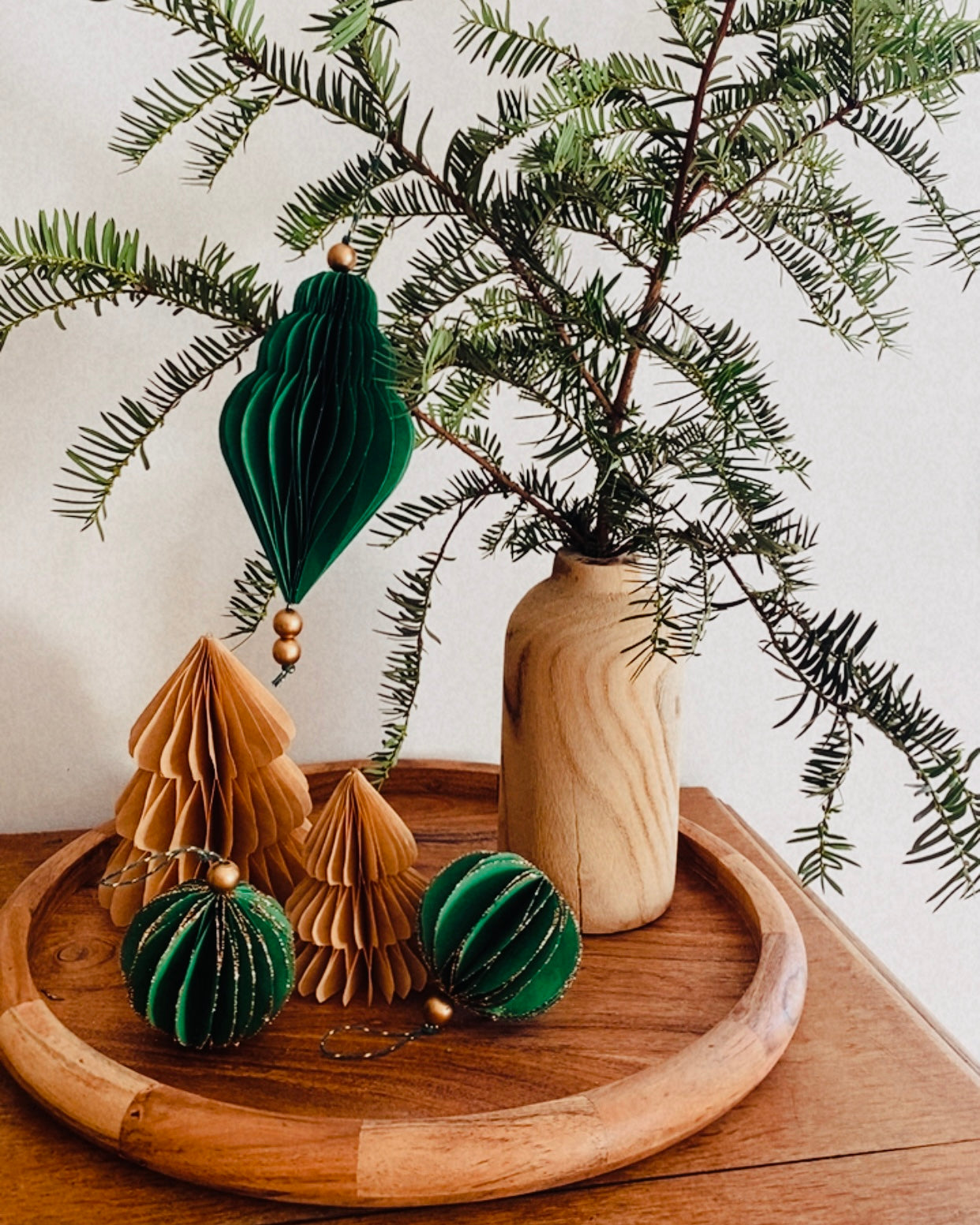 Ornements de Noël faits main en papier, présentés dans une coupe en bois garnie de branches de sapin. Les boules sont de différentes formes et couleurs : vert émeraude profond et écru chaleureux. Certaines sont rehaussées de fines paillettes dorées. L’ensemble évoque une décoration naturelle, authentique et poétique, parfaite pour un Noël doux, artisanal et inspiré par la nature. ninona