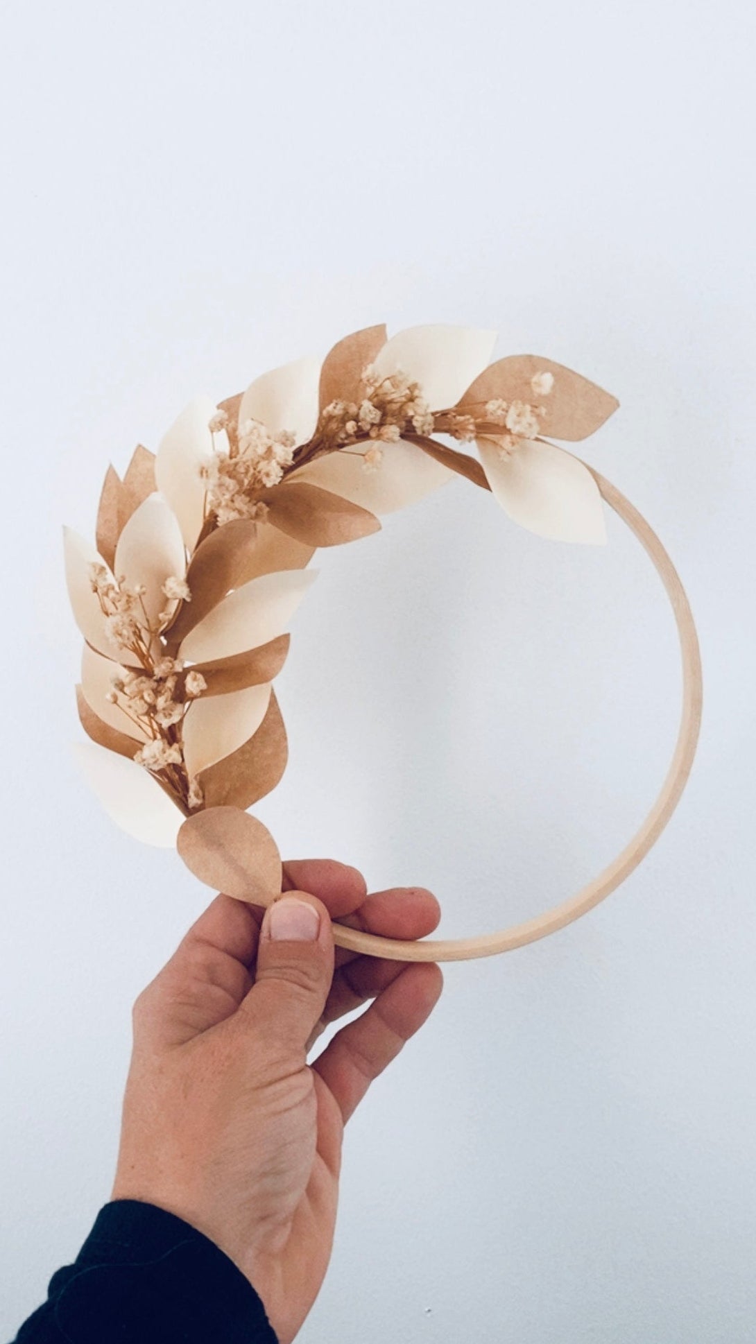 Couronne décorative faite main avec un anneau en bois, des pétales en papier tons écru et marron clair, et des touches de gypsophile séchée. Une création artisanale minimaliste et chaleureuse, parfaite pour la décoration d’un intérieur, d’une chambre d’enfant ou d’un mariage. Possibilité d’ajouter un mot ou prénom en fil de laiton pour une personnalisation unique et élégante. ninona