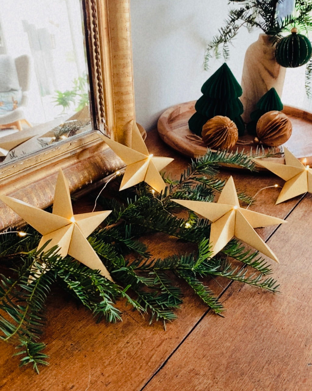 Guirlande d’étoiles en papier doré fixée près d’un miroir ancien. Lumière LED douce créant une ambiance chaleureuse et accueillante. Chaque étoile est réalisée à la main avec soin, inspirée de l’artisanat et de la décoration naturelle. Parfait pour le salon, une chambre d’enfant, ou pour créer une atmosphère de Noël douce et lumineuse. Décoration élégante et poétique. ninona