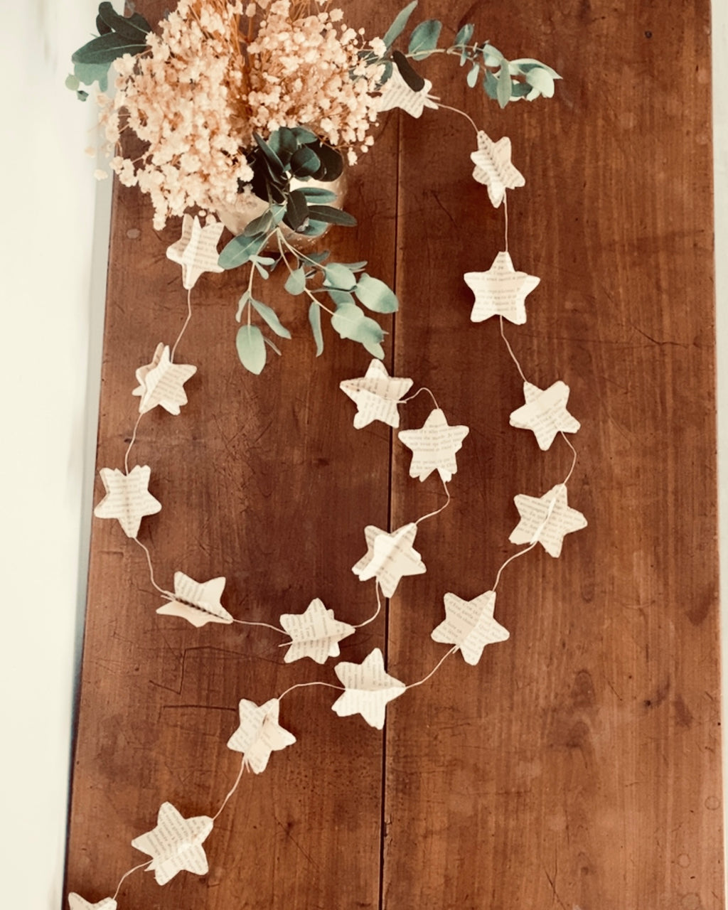 Gros plan sur les étoiles en papier recyclé. Chaque étoile est formée manuellement à partir de pages de livres, ce qui rend chaque guirlande unique. Le rendu est poétique, doux et artisanal. Cette guirlande s’intègre facilement à un intérieur chaleureux, scandinave, vintage ou minimaliste. ninona