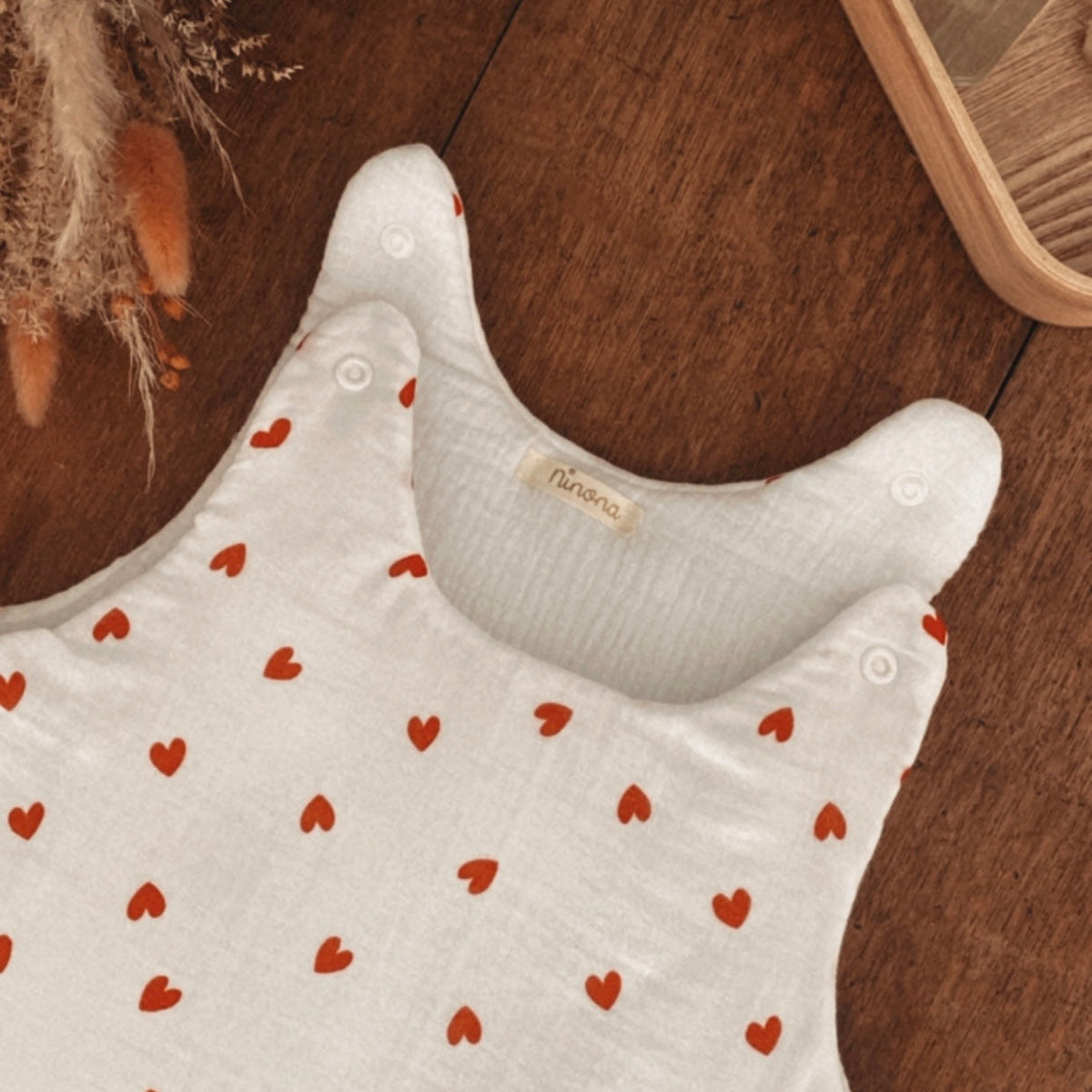 Détail des pressions aux épaules d’une gigoteuse bébé en double gaze de coton écrue à petits cœurs rouges. Les ouvertures permettent de faciliter l’installation de bébé dans la turbulette et de mieux voir les finitions du modèle. L’intérieur est lui aussi en double gaze de coton, pour conserver une sensation douce et confortable. Cette gigoteuse d’hiver est proposée en taille 0/6 mois avec un TOG 2, idéale pour la saison froide. Une finition délicate qui souligne le soin apporté à chaque détail.