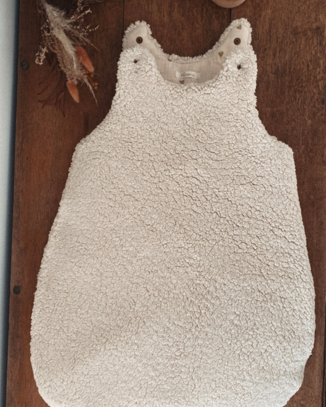 Gigoteuse d’hiver en sherpa et double gaze de coton pour bébé, coloris écru naturel avec petits cœurs beige. Confortable, chaude et respirante, elle offre un cocon douillet idéal pour les nuits hivernales. Fermeture pratique par pressions aux épaules. Parfaite comme cadeau de naissance ou pour assurer des nuits paisibles à bébé tout en douceur. Style bohème, matières naturelles et moelleuses