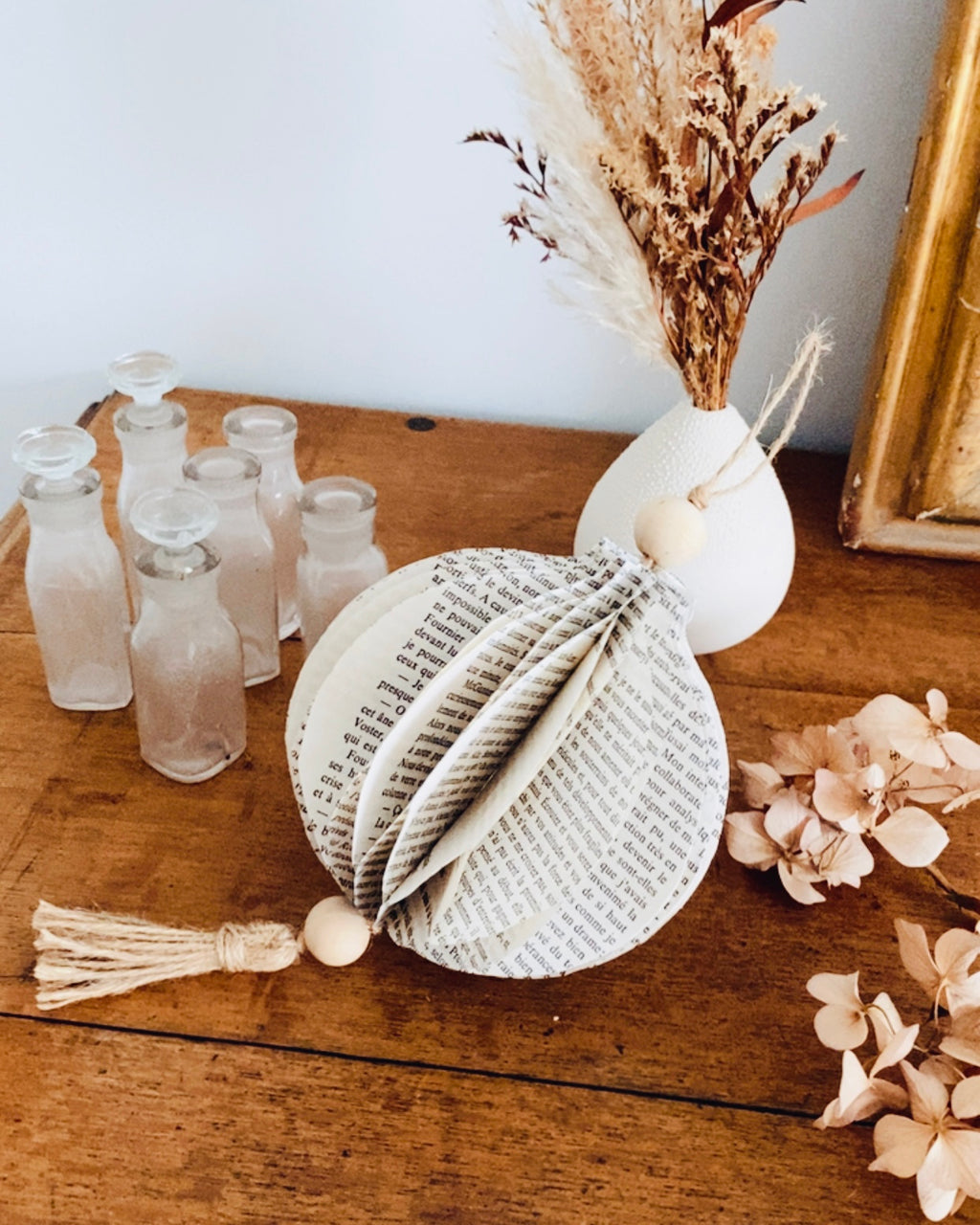 Offrez une seconde vie aux mots avec cette boule décorative en papier recyclé. Réalisée à la main à partir de vieux livres, elle allie élégance et durabilité. Sa ficelle naturelle et ses perles de bois en font une création unique et responsable. Parfaite pour une déco bohème, poétique ou minimaliste, elle sublime votre intérieur avec douceur. ninona