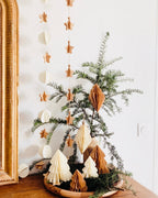 Petit sapin en papier fait main, présenté en décor de Noël naturel. Chaque pièce est unique, réalisée avec soin artisanal. Ces sapins décoratifs ajoutent une touche chaleureuse et poétique, idéale pour une décoration de table ou une ambiance douce et hivernale dans la maison. ninona