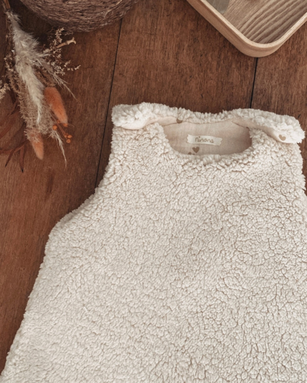 Gigoteuse d’hiver en sherpa et double gaze de coton pour bébé, coloris écru naturel avec petits cœurs beige. Confortable, chaude et respirante, elle offre un cocon douillet idéal pour les nuits hivernales. Fermeture pratique par pressions aux épaules. Parfaite comme cadeau de naissance ou pour assurer des nuits paisibles à bébé tout en douceur. Style bohème, matières naturelles et moelleuses