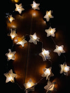 Guirlande décorative faite main composée de 20 étoiles en papier recyclé, decoupées dans de vieilles pages de livres. Chaque étoile est en volume pour créer un effet léger et poétique. La guirlande apporte une ambiance douce, qu’elle soit allumée ou simplement suspendue. Idéale pour une décoration bohème, vintage ou chaleureuse dans un salon, une chambre ou un espace détente. ninona