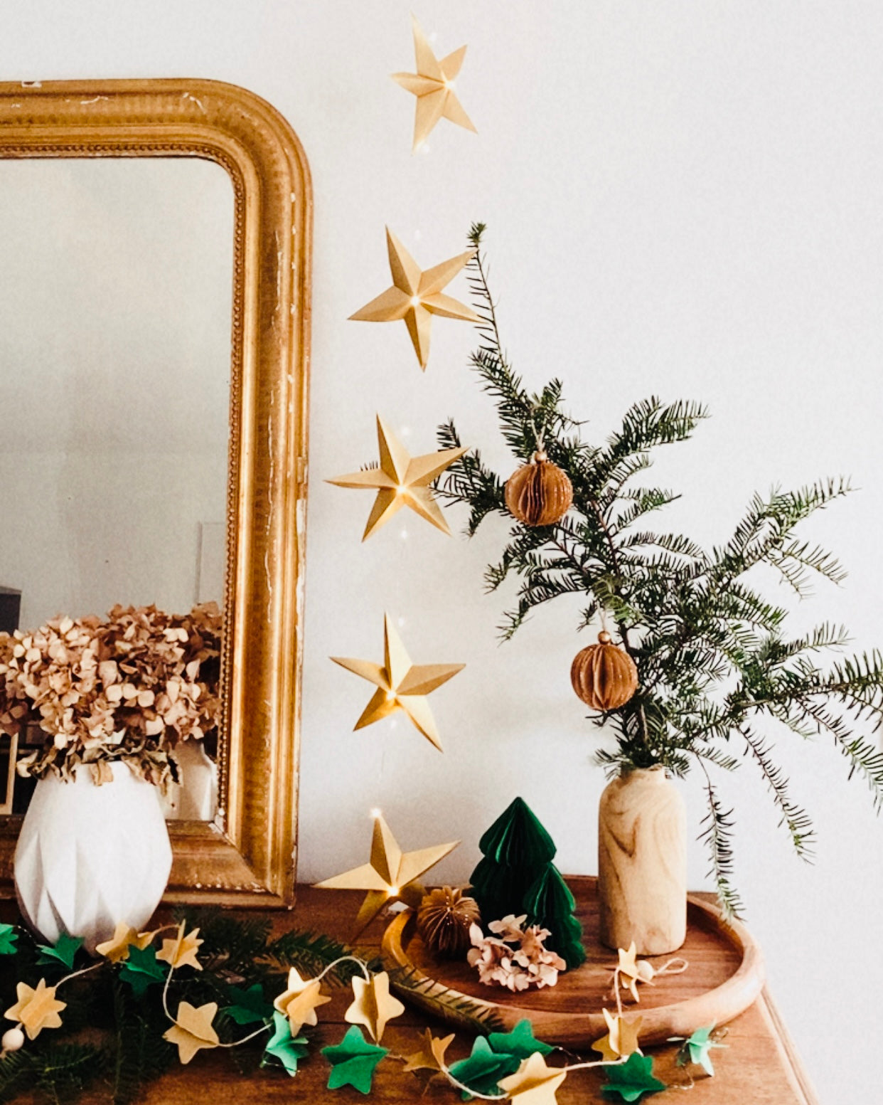 Guirlande d’étoiles en papier doré fixée près d’un miroir ancien. Lumière LED douce créant une ambiance chaleureuse et accueillante. Chaque étoile est réalisée à la main avec soin, inspirée de l’artisanat et de la décoration naturelle. Parfait pour le salon, une chambre d’enfant, ou pour créer une atmosphère de Noël douce et lumineuse. Décoration élégante et poétique. ninona