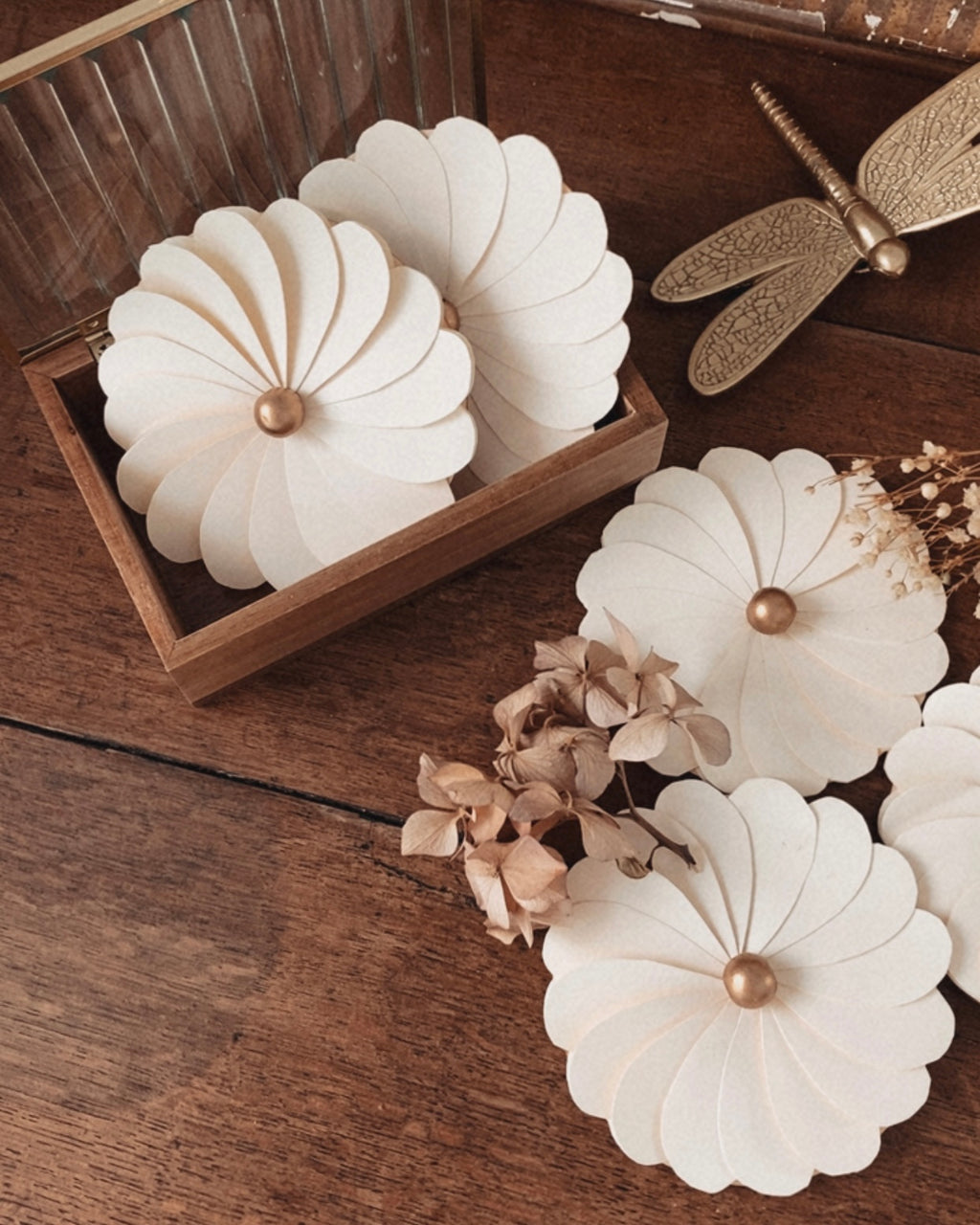 Ensemble de fleurs en papier écru disposées dans et autour d’un coffret en bois, créant une composition décorative raffinée et poétique. Les pétales délicatement superposés et les cœurs en perle de bois soulignent l’élégance de cette décoration artisanale. Ces fleurs en papier sont idéales pour décorer une table de mariage, un événement festif ou pour composer une décoration murale douce et intemporelle dans un intérieur. ninona creation