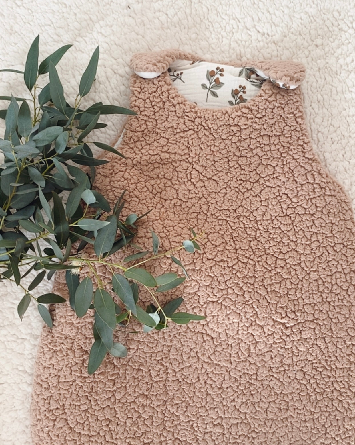 Gigoteuse d’hiver artisanale en sherpa beige, doublée en double gaze de coton imprimée de petites branches florales. Avec son indice TOG 2, elle garde bébé bien au chaud tout l’hiver. Convient aux bébés de 0 à 6 mois. Son style doux et naturel s’intègre parfaitement dans une chambre de bébé apaisante. Cette gigoteuse faite main est un cadeau de naissance idéal, mêlant esthétique, confort et sécurité pendant le sommeil.