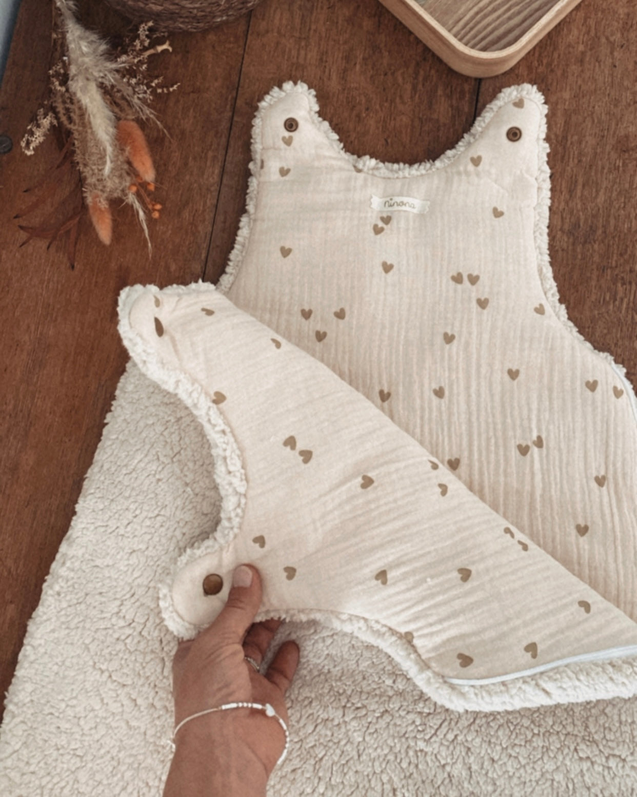 Gigoteuse d’hiver en sherpa et double gaze de coton pour bébé, coloris écru naturel avec petits cœurs beige. Confortable, chaude et respirante, elle offre un cocon douillet idéal pour les nuits hivernales. Fermeture pratique par pressions aux épaules. Parfaite comme cadeau de naissance ou pour assurer des nuits paisibles à bébé tout en douceur. Style bohème, matières naturelles et moelleuses