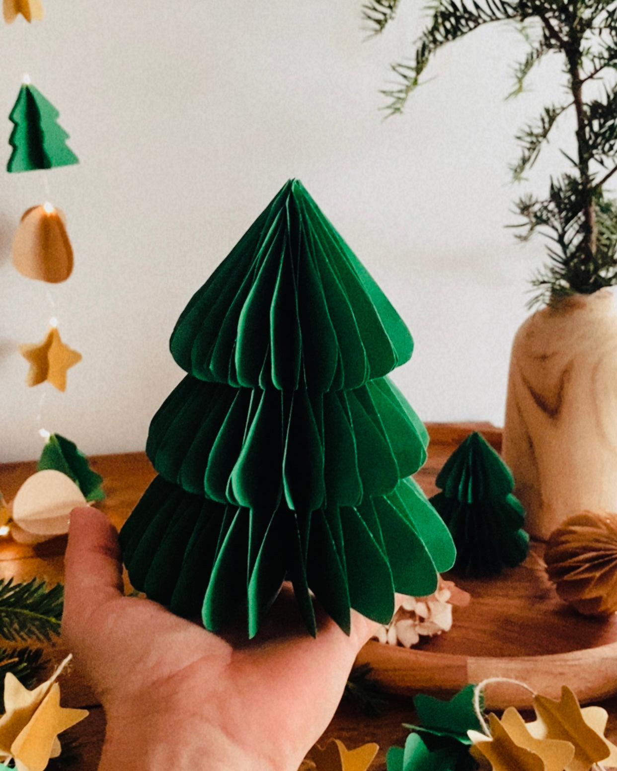 Lot de deux sapins en papier faits main, en vert émeraude, posés sur un plateau en bois dans une ambiance douce et chaleureuse. Ces décorations artisanales de Noël apportent une touche poétique et naturelle à votre intérieur. Idéal pour compléter une décoration de table, créer un village d’hiver miniature ou offrir un cadeau fait avec soin. ninona
