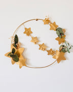 Couronne faite main en atelier français, associant eucalyptus, petites fleurs séchées blanches et étoiles dorées sur un cercle en métal. Présentée avec socle en bois. Décoration idéale pour Noël, une table de fête ou une décoration intérieure douce et naturelle. Convient également toute l’année pour créer une ambiance chaleureuse et apaisante. Cadeau authentique et unique à offrir ou à s’offrir. ninona