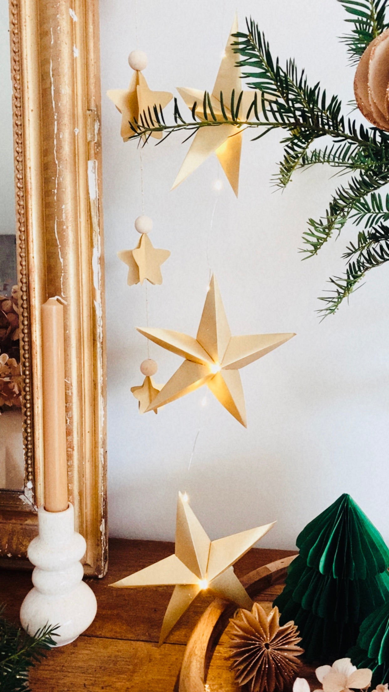 Guirlande d’étoiles en papier doré fixée près d’un miroir ancien. Lumière LED douce créant une ambiance chaleureuse et accueillante. Chaque étoile est réalisée à la main avec soin, inspirée de l’artisanat et de la décoration naturelle. Parfait pour le salon, une chambre d’enfant, ou pour créer une atmosphère de Noël douce et lumineuse. Décoration élégante et poétique. ninona