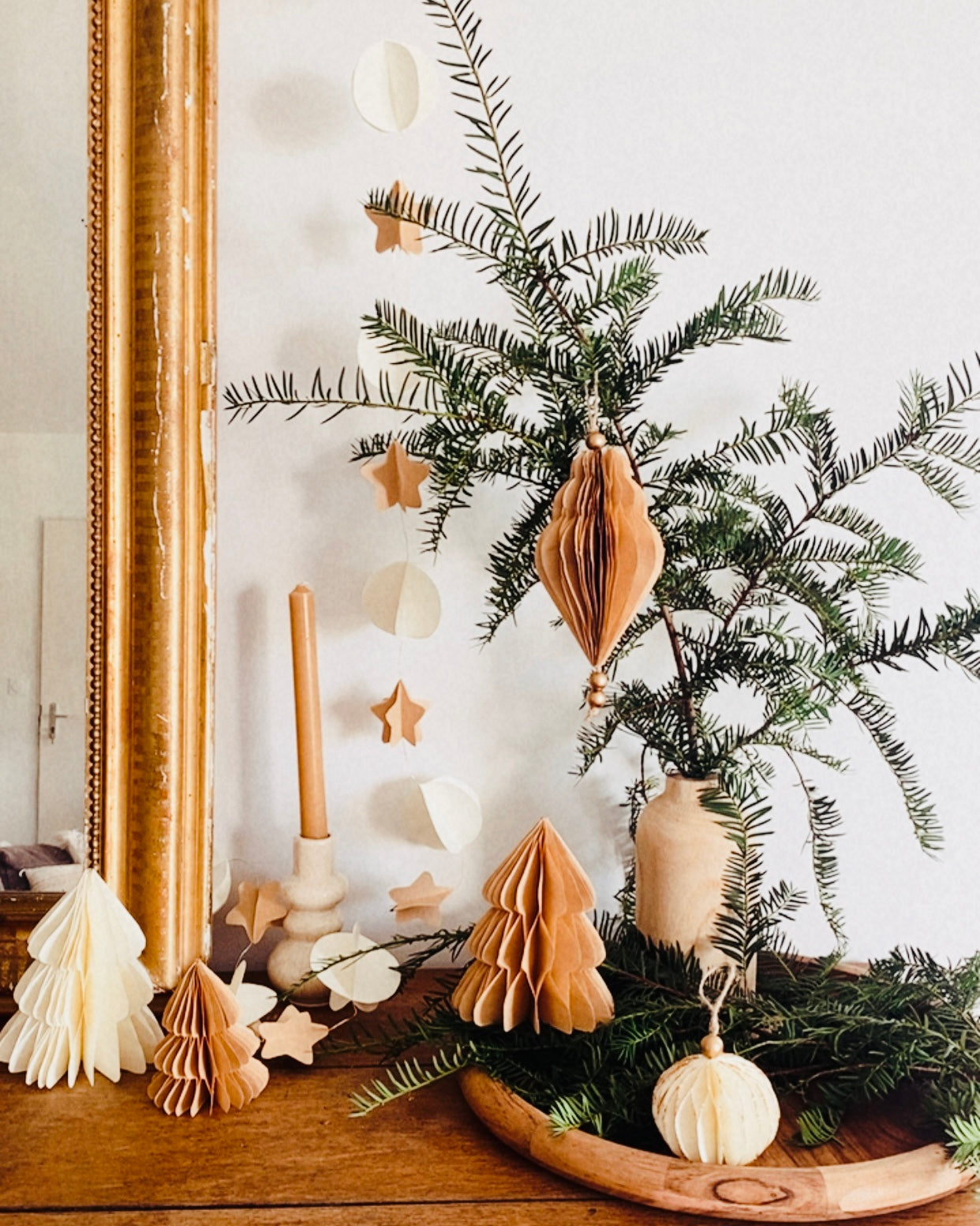 Décoration de Noël artisanale en papier, suspendue par une cordelette naturelle avec une perle dorée. La boule présente une forme élégamment travaillée en plusieurs couches découpées à la main, avec de légères touches de paillettes dorées qui soulignent ses contours. L’ornement, de teinte écru douce, est tenu dans une main, mettant en valeur son relief, sa finesse et son allure poétique, idéale pour décorer un sapin ou une guirlande de fête. ninona