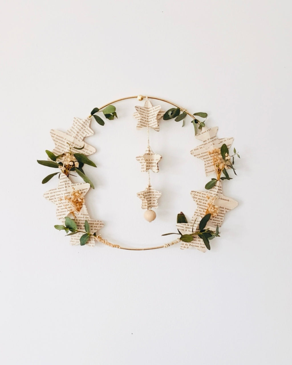 Couronne décorative artisanale réalisée à la main avec des pages de vieux livres découpées en forme d’étoiles, associées à de l’eucalyptus séché et de la gypsophile. Cette création poétique peut être suspendue ou posée, pour une décoration naturelle et chaleureuse. Idéale pour une décoration de Noël douce et lumineuse ou pour agrémenter la maison toute l’année. Une pièce d’artisanat français unique, bohème et pleine de charme, faite avec soin. ninona