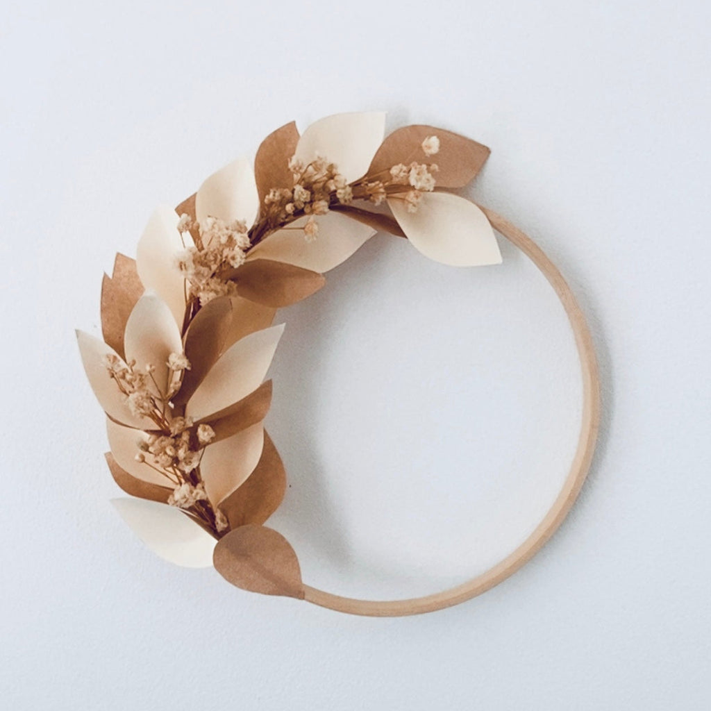 Couronne artisanale en papier écru et marron clair, composée de pétales découpés et collés à la main, avec des brins de gypsophile séchée. Fixée sur un cercle en bois, elle offre un style naturel, poétique et épuré. Idéale comme décoration murale, objet bohème ou pièce personnalisable avec un prénom en fil de laiton pour une chambre, un événement ou un cadeau unique. ninona