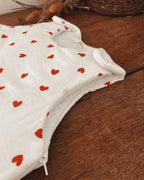 Vue rapprochée de la gigoteuse bébé écrue à petits cœurs rouges, mettant en valeur la texture souple et légèrement gaufrée de la double gaze de coton. On aperçoit la fermeture éclair latérale ainsi que les finitions du bas arrondi. Ce modèle est une gigoteuse d’hiver TOG 2, disponible en taille 0/6 mois. Conçue pour offrir douceur et confort pendant les nuits fraîches, elle se distingue par son motif de petits cœurs. Une ouverture pratique pour installer bébé facilement et préserver son confort.