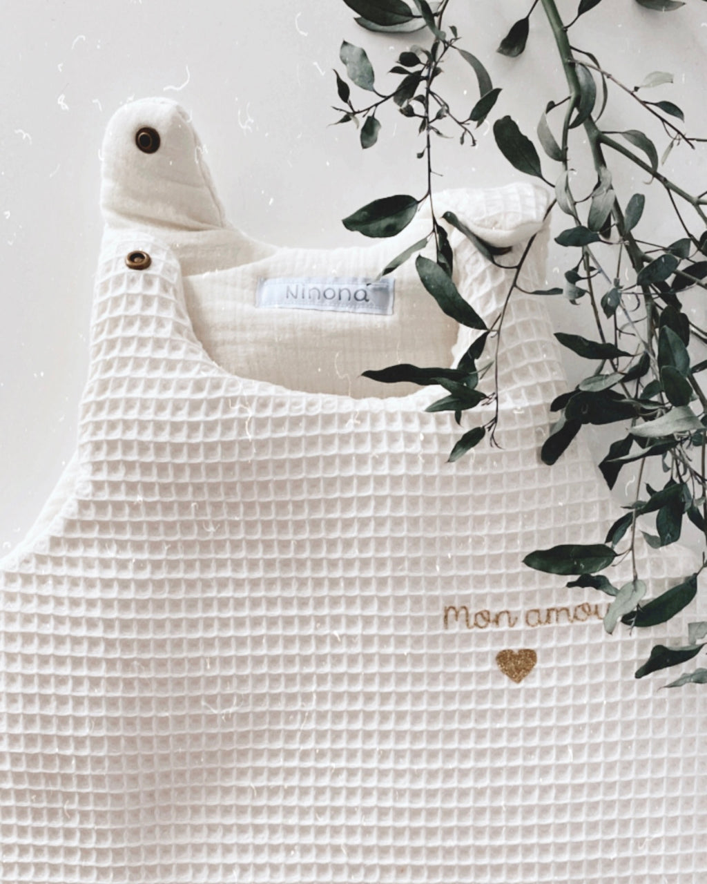 Chez Ninona, chaque gigoteuse est pensée et fabriquée avec amour. Ce modèle en nid d’abeille et double gaze de coton écru offre confort et légèreté pour des nuits paisibles. Conçue pour assurer sécurité et chaleur, elle devient vite un indispensable du trousseau de naissance. Brodée au prénom de votre choix, la gigoteuse Ninona est une création artisanale, unique et personnalisée, parfaite pour chérir bébé dès ses premiers instants.