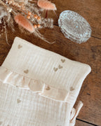 protège carnet de santé personnalisable, dans les tons beiges et écru. Cette housse de carnet de sante personnalisable est réalisée avec une double gaze de coton, avec des petits coeurs dorés.  De jolis froufrou ajoutent une touche de poèsie à cette housse de carnet de santé. Idéal comme cadeau de naissance pour une petite fille.