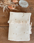 protège carnet de santé personnalisable, dans les tons beiges et écru. Cette housse de carnet de sante personnalisable est réalisée avec une double gaze de coton, avec des petits coeurs dorés.  De jolis froufrou ajoutent une touche de poèsie à cette housse de carnet de santé. Idéal comme cadeau de naissance pour une petite fille.